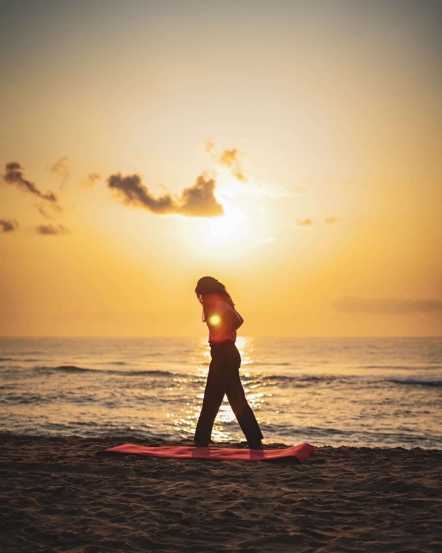 Instructor silhouetted against the sunset on a beach yoga mat