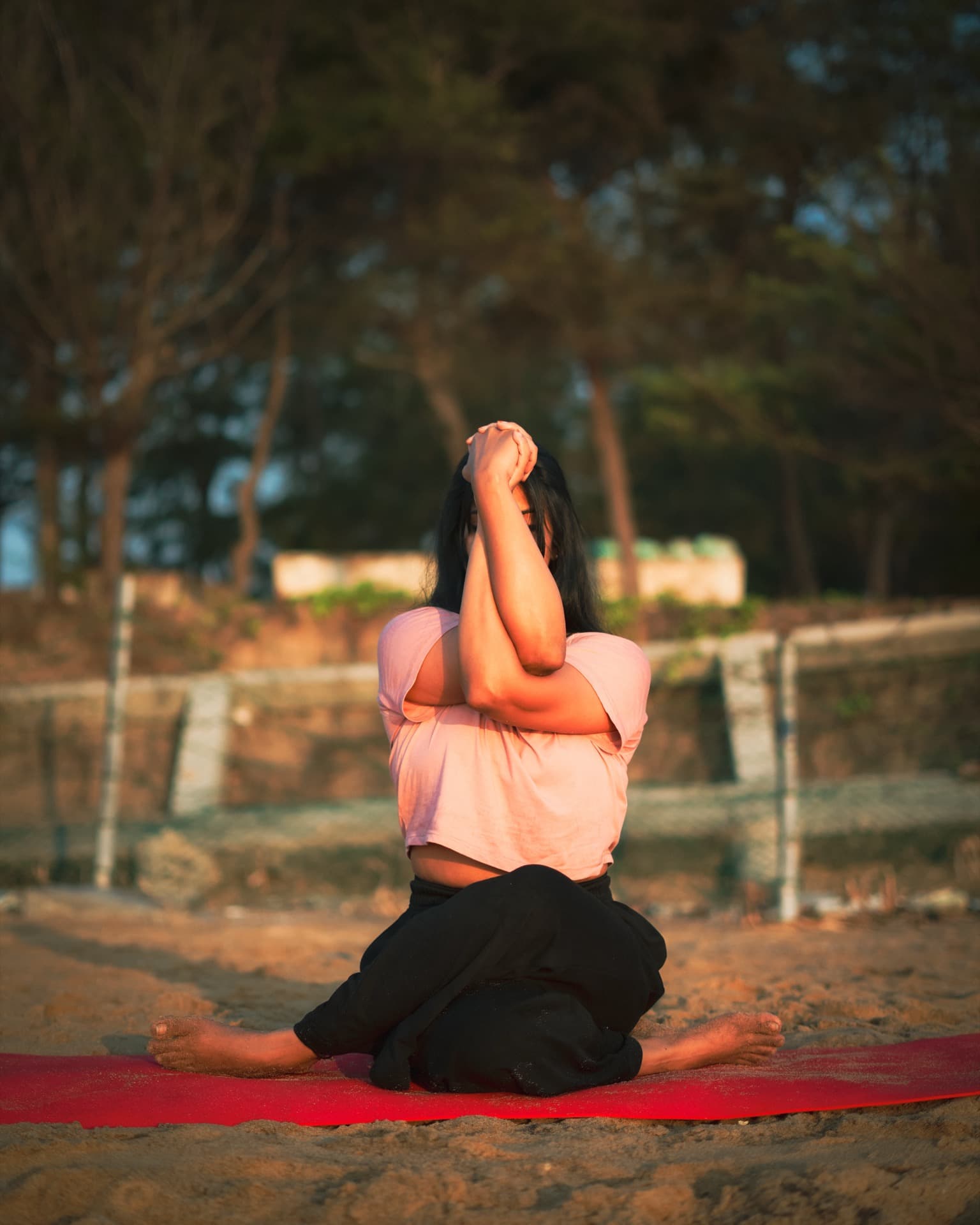 Ashwitha seated in cow-face pose at sunset on the beach